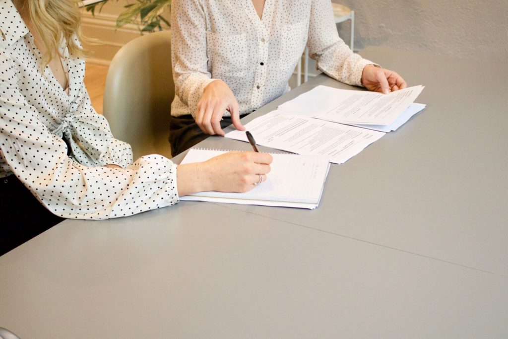 Two people reviewing paper. One person holding pen and writing.