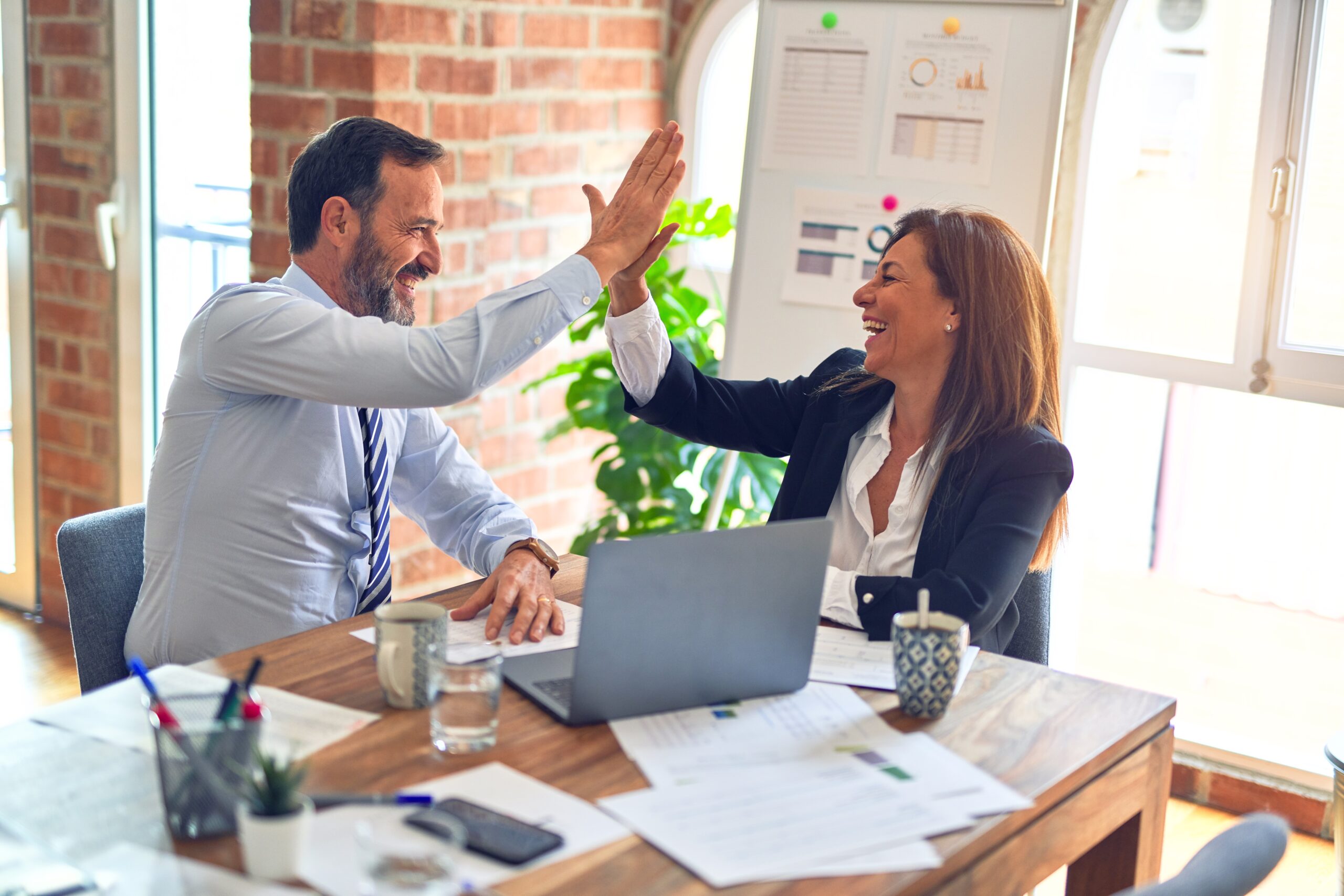 Man and woman high fiving while working on computer.