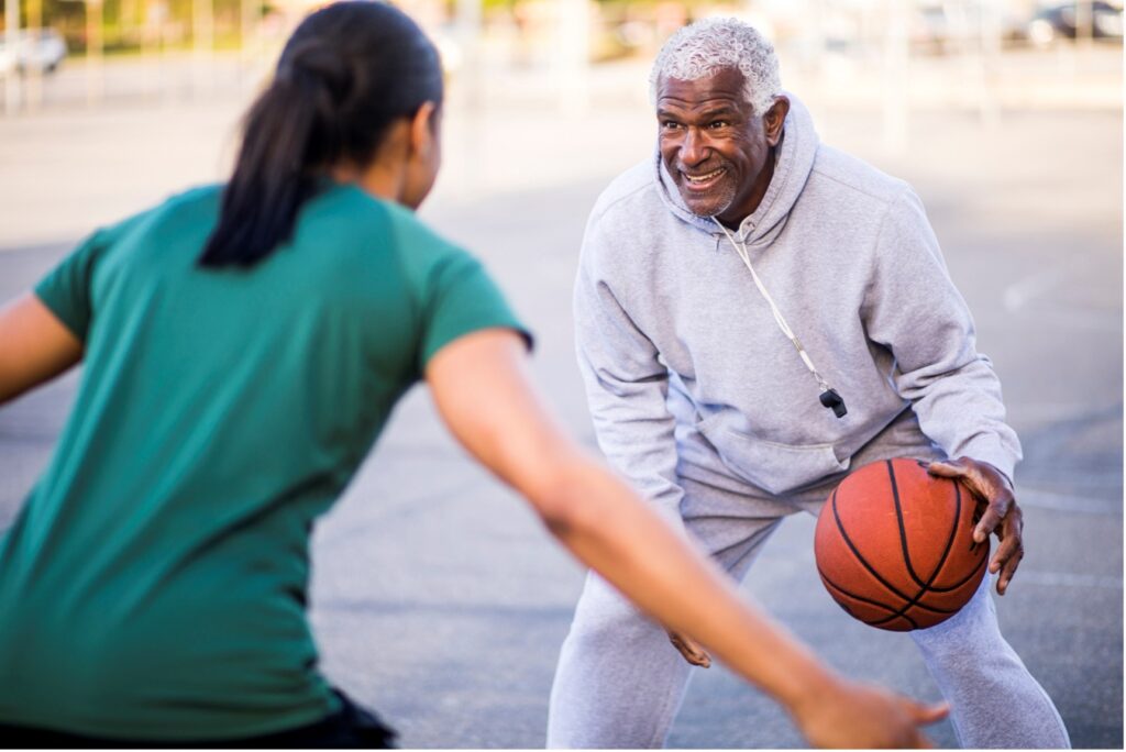 Woman playing basketball with elderly man.