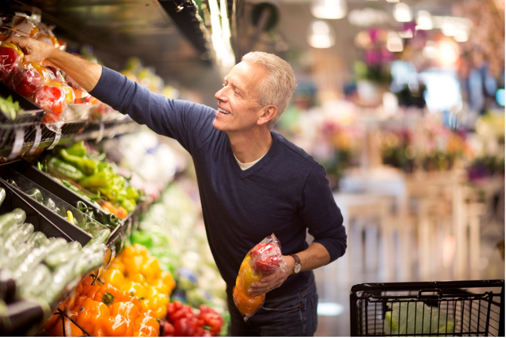 Man in produce section of grocery store holding bell peppers.